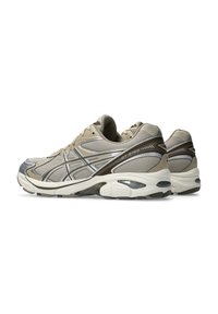 Beige athletic shoes with mesh upper, reflective accents, cushioned sole, and a durable rubber outsole. Features a sleek, rounded design.