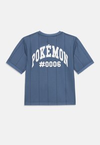 Mėlyna trumpomis rankovėmis esančio marškinėlių su vertikaliomis juostelėmis. Ant nugaros didelėmis baltomis raidėmis užrašyta „POKÉMON“ ir „#0006“. Laisvas kirpimas.