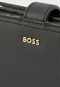 Čierna kožená peňaženka s textúrovaným povrchom, jemným prešitím a zlatým logom „BOSS“. Kompaktný dizajn s horným remienkom.