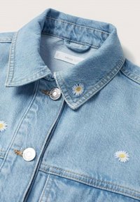 Ljusblå denimjacka med klassisk krage, två silverknappar och vit prästkragebroderi på framsidan.