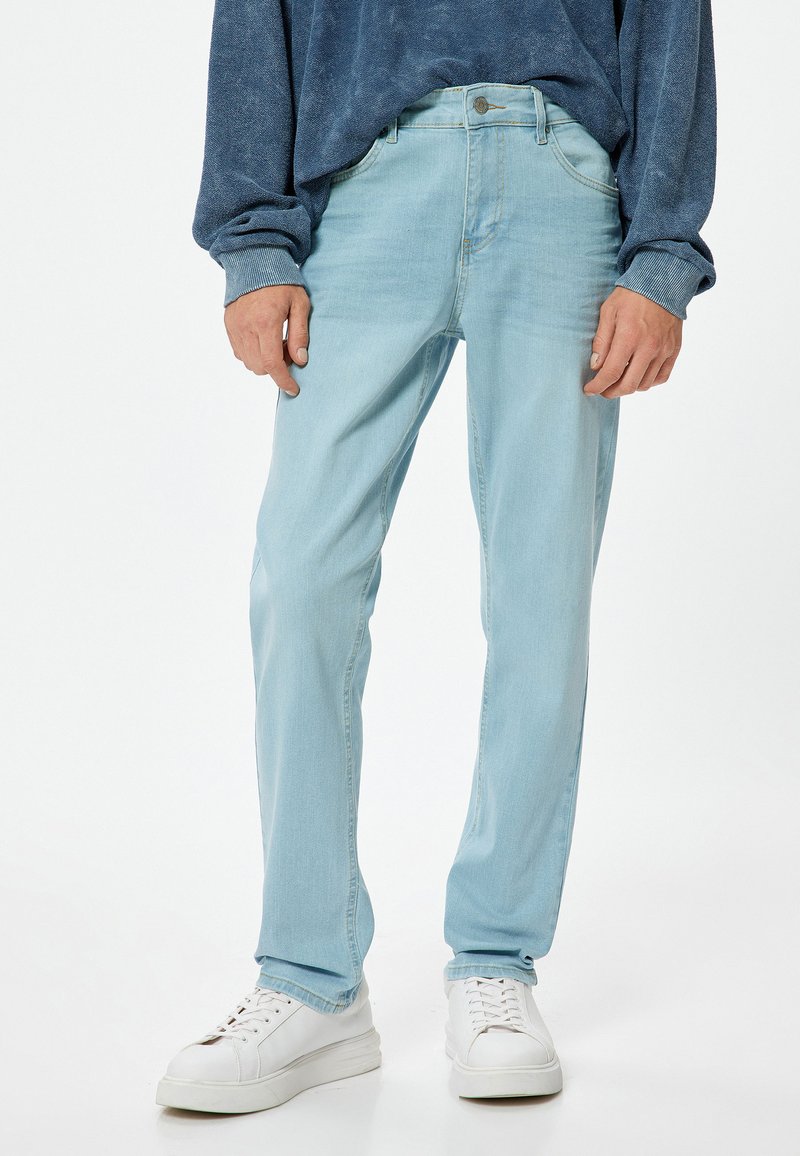 Vaqueros de mezclilla azul claro con corte recto, que cuentan con cinco bolsillos y costuras sutiles. Combinados con zapatillas blancas y una camiseta de manga larga azul.