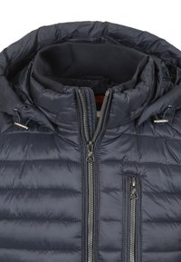 Marineblauwe pufferjas met een rits aan de voorkant, hoge kraag en twee ritszakken. De stof heeft een doorgestikte textuur en metalen accenten.