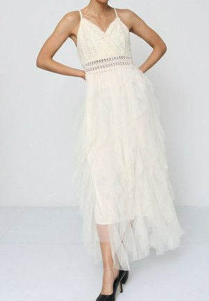 Robe ivoire avec un corsage ajusté mettant en valeur des motifs brodés, une taille en crochet et une jupe en tulle superposée. Bretelles spaghetti réglables.