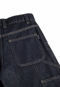 Σκούρο μπλε τζιν με ορατό κίτρινο ράψιμο, πίσω τσέπη, θηλιές για ζώνη και μια μικρή ασπρόμαυρη υφασμάτινη ετικέτα.