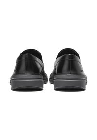 Par de zapatos de cuero negro sin cordones vistos desde atrás con suelas de goma negra gruesa sobre un fondo blanco.