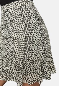 Plisovaná sukně v krémové barvě s černým abstraktním květinovým vzorem. Lehce průhledná látka, délka po kolena se splývavým lemem, s přiléhavým pasem.