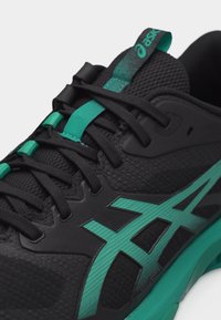 Κοντινό πλάνο μαύρου και μπλε-πράσινου αθλητικού παπουτσιού Asics, που δείχνει τα κορδόνια, το διχτυωτό ύφασμα και το λογότυπο στη πλευρά και τη γλώσσα.