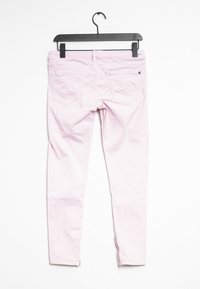 Jeans skinny color rosa claro con una textura suave, que cuentan con dos bolsillos traseros y cremalleras en los tobillos, colgados en una percha negra.