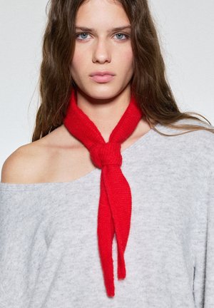 Sciarpa rossa lavorata a maglia annodata al collo, realizzata in materiale morbido. Indossata sopra una maglietta grigia a spalle scoperte, con una vestibilità comoda e tessuto texturizzato.