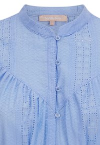 Blouse bleu clair avec un motif texturé, col rond et fermeture à boutons. Présente un design froncé et des détails semblables à de la dentelle.