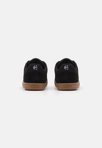 Black suede skate shoes with a brown rubber sole. Features include a padded collar and heel with a logo accent on the back.