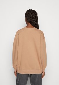 Beige sweatshirt med avslappnad passform, rund halsringning och ribbad mudd, tillverkad av mjukt bomullsblandat tyg med en enkel design.