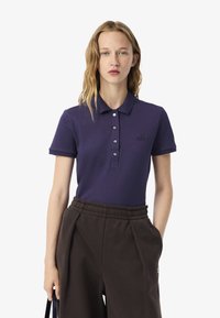 Polo shirt blu navy in cotone con una patta con tre bottoni e logo ricamato. Abbinato a pantaloni della tuta marrone scuro con vita elasticizzata.