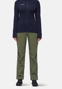 Veste en polaire zippée bleu marine avec manches longues, associée à un pantalon tapered vert olive et des bottes de randonnée noires. Tissu texturé, design fonctionnel.