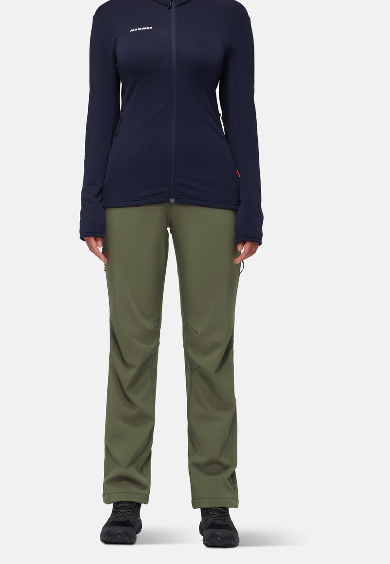 Veste en polaire zippée bleu marine avec manches longues, associée à un pantalon tapered vert olive et des bottes de randonnée noires. Tissu texturé, design fonctionnel.