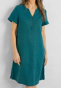 Vestido de lino en tono verde azulado con mangas cortas con vuelta, escote en V y botonera. Corte recto hasta la rodilla con aberturas laterales para mayor movilidad.