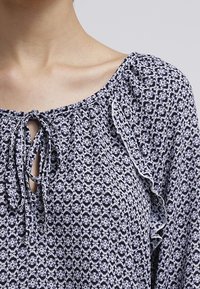 Blouse marine et blanche à motifs, dotée d'un col à nouer et de bords festonnés, fabriquée dans un tissu léger au fini texturé.