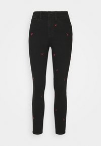 Pantalones ajustados negros con pequeños bordados de rosas rojas dispersos por la tela, con bolsillos frontales y trabillas para cinturón.