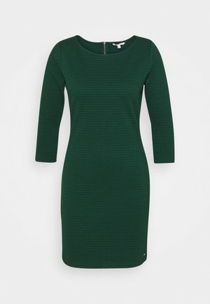 Robe verte avec un motif texturé, encolure bateau et manches trois-quarts. Elle dispose d'une fermeture éclair au dos et d'une silhouette cintrée.