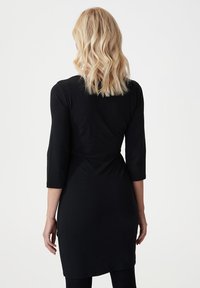 Černé šaty ke kolenům vyrobené z měkké, elastické tkaniny. Mají tříčtvrteční rukávy a přiléhavý pas pro upravený siluetu.