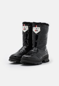 Bottes d'hiver noires imperméables avec un design matelassé, une bordure en fausse fourrure, une semelle en caoutchouc et une étiquette de marque ornée d'un blason et d'accents du drapeau français.