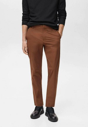 Brown tailored pants made of smooth fabric, featuring side pockets, a slim fit, and paired with black shoes.