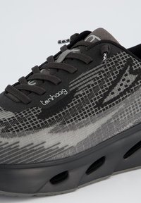 Chaussure de sport noire avec un dessus texturé arborant des motifs géométriques gris, des lacets ronds et une semelle épaisse et rembourrée avec des ports de ventilation.