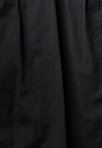 Tissu noir à surface texturée ; motifs cousus subtils créant des lignes verticales. Le matériau semble doux et léger.