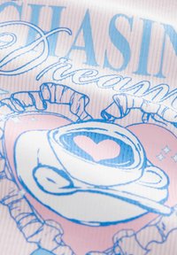 Grafisk T-shirt med ribbet tekstur, der viser blå tekst "Chasing Dreams" og en hjerteformet kaffekop mod en pink baggrund.