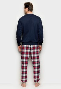 Conjunto de pijama para hombre que incluye una camiseta azul marino de cuello redondo y pantalones de franela a cuadros en rojo, blanco y negro con cinturilla elástica. Material de algodón.