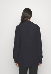 Marinblå stickad cardigan med långa ärmar, texturerat tyg, rundad krage och en något längre bakfald för en avslappnad passform.