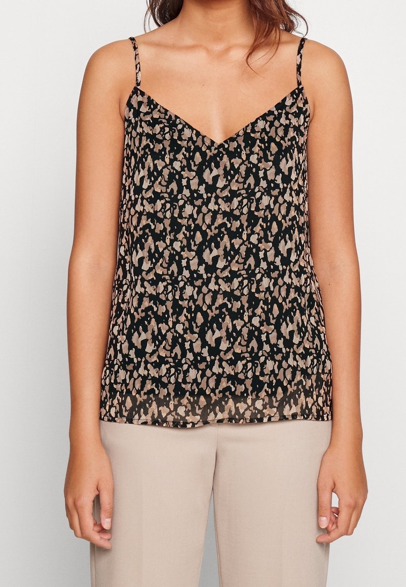 Camisole noire transparente à encolure en V ; présente un motif abstrait beige et marron et des bretelles fines réglables. Associée à un pantalon de couleur claire.
