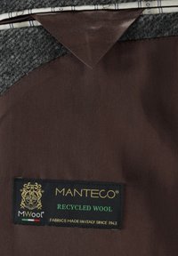 Manteco Markenstoffetikett auf braunem Stoff, Text lautet "Recycelte Wolle" und "Stoffe hergestellt in Italien seit 1943."