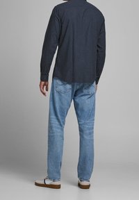 Tmavě modrá košile s dlouhým rukávem a knoflíkovými manžetami, v kombinaci se světlomodrými džíny rovného střihu a bílými teniskami s hnědými podrážkami.