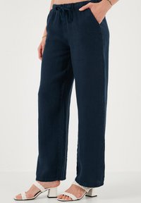 Navyblauwe, wijde broek met een trekkoord in de taille en zijzakken, gemaakt van lichtgewicht stof. Gekoppeld met witte hakken sandalen.