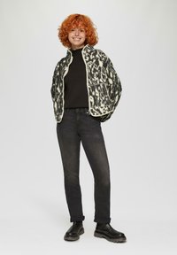 Zwart-wit gestreepte fleece jack met hoge kraag en twee voorzakken, gedragen over een zwarte top, gecombineerd met donkere jeans en zwarte laarzen.