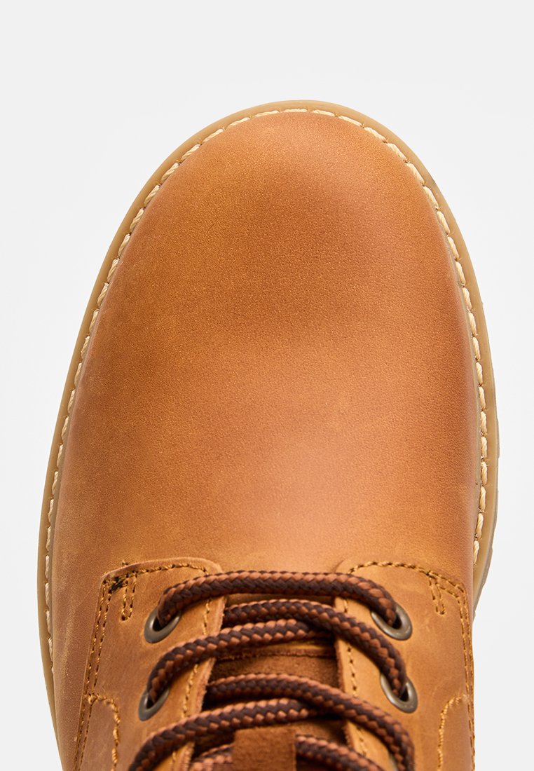 Botte en cuir tan avec un bout rond, des lacets marron et des coutures contrastantes le long de la semelle. Texture lisse avec des accents minimes.