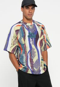 Farverig oversized t-shirt med et tekstureret strikmønster i blå, orange og grøn nuancer. Sort logoaccent på forsiden.