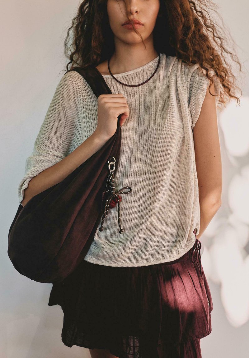 Jasnobeżowy dzianinowy top z krótkimi rękawami w połączeniu z ciemnobrązową plisowaną mini spódnicą. Torebka zdobiona ozdobnym zawieszkiem z czerwonymi akcentami.