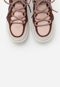 Béžové a vínové tenisky s hladkou texturou, mají kulatou špičku, vzorované tkaničky a žluté akcenty na okách.