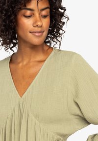 Lichtgroene gebreide blouse met een v-hals, geraffineerde details aan de voorkant en volumineuze mouwen.