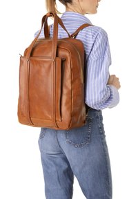 Zaino in pelle marrone con doppie maniglie superiori e spallacci regolabili. Presenta una chiusura con zip e una tasca frontale. Design semplice e strutturato.