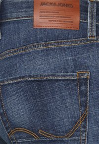 Mörkblå denimjeans med orange sömdetaljer, med en läderetikett på midjebandet som står "JACK & JONES."
