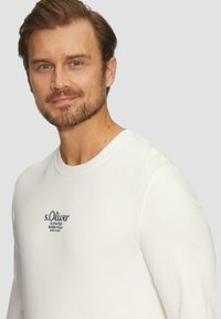 Witte lange mouwen t-shirt met een ronde hals en een zachte textuur, voorzien van een geborduurd zwart logo op de borst.