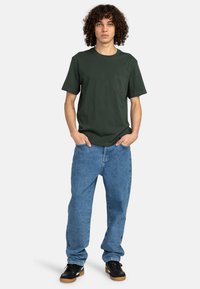 Grøn kortærmet t-shirt med brystlomme, parret med løse blå denimjeans og sorte sneakers med gummisåler.
