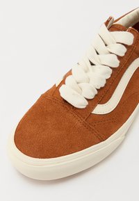 Baskets en suede marron avec des lacets crème et des accents sur les côtés, présentant un bout arrondi et une semelle en caoutchouc texturée.