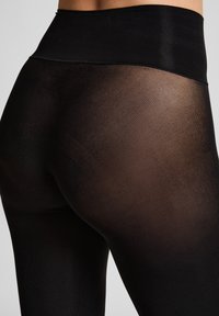 Hochtaillierte schwarze Leggings aus einer Mischung von transparentem und opakem Material, mit einer glatten Textur und einem dehnbaren Design für Komfort und Passform.