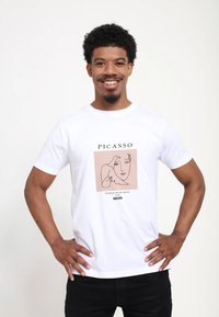 Hvid bomuld t-shirt med et Picasso stregtegning af en kvinde og en due, med teksten "PICASSO," "KVINDE MED DUE," og "1949."