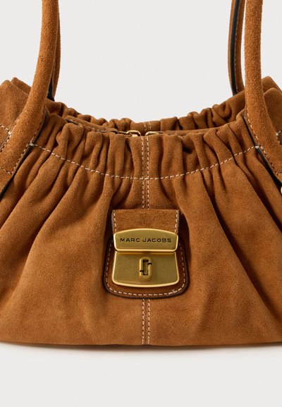 Pruun seemisnahast käekott, millel on volditud disain, kuldsed detailid ja ristkülikukujuline lukk, millele on graveeritud "MARC JACOBS". Õmmeldud aktsendid on nähtavad.