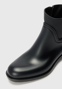 Black ankle boot made of smooth, glossy material with a sleek design, featuring a rounded toe and minimal detailing.